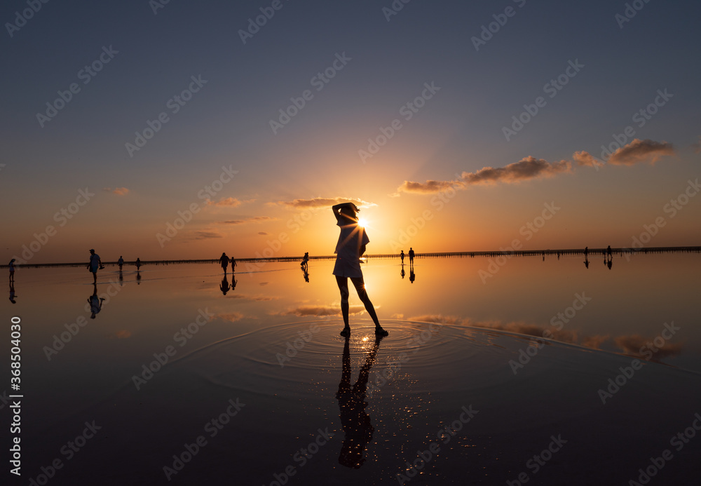 Fototapeta premium Beautiful sunset on the lake, the sun reflecting in the water, silhouette of a girl in the middle