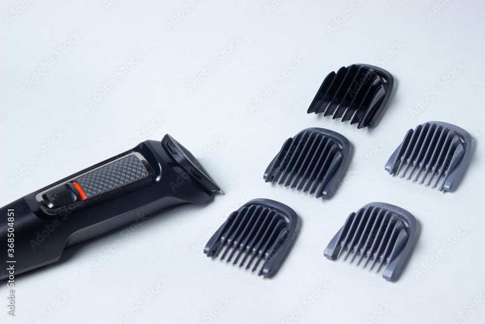 Fototapeta premium Beard trimmer on a white background. Different sized attachments are placed next to the trimmer. Beard care. Male style