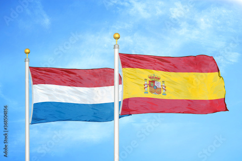 Netherlands and Spain two flags on flagpoles and blue sky