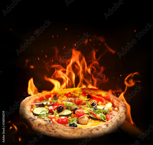 Hot tasty pizza with fire flames on dark background. Image for menu or poster photo