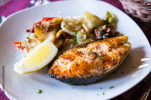 delicious salmon steak with potato garnish with slice of lemon on white plate in restaurant