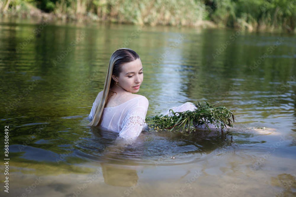 Fototapeta premium Young white woman with long blondy hair in a river in a forest in summer