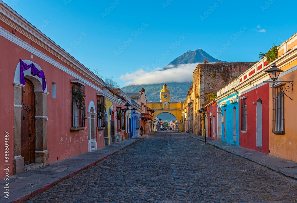 Cityscape of Antigua city at sunrise with Santa Catalina arch and Agua volcano, Guatemala.