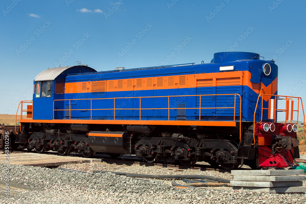 a blue shunting diesel locomotive with an orange stripe, a deck type locomotive stands on a railroad bed strewn with rubble, nobody. a blue shunting diesel locomotive with an orange stripe, a deck type locomotive stands on a railroad bed strewn with rubble, nobody.