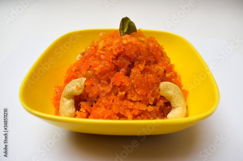 Selective focus of Gajar ka Halwa, a popular Indian, Pakistani sweet dish dessert, made of grated carrot. Garnished iwth cashewnuts, pista, dry fruits in a yellow bowl ready to serve hot or cold photo