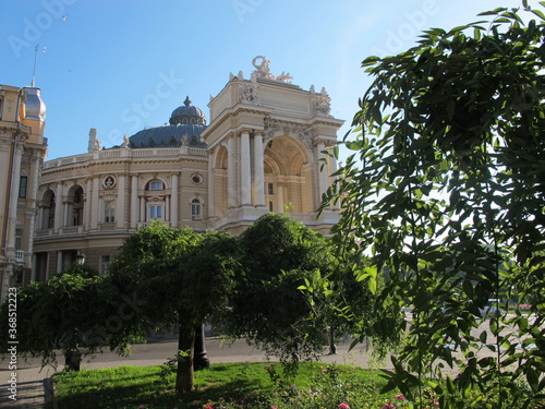 The old building of the Odessa Opera and Ballet Theater on a clear sunny summer morning, architects Fellner and Helmer, the style of the new Viennese Baroque. Beautiful green trees in front of the the photo