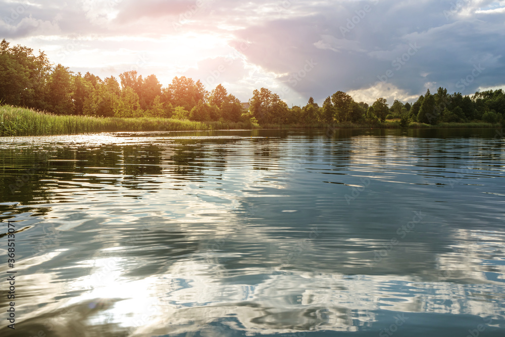 Naklejka premium Summer landscape: the sky with clouds and the forest on the horizon are reflected in the clear water of the lake. Copspace. The concept of a relaxing holiday, the beauty of nature.