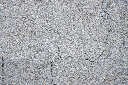 White plaster painted wall with curvy crack. Cracked wall closeup photo. Architecture detail background. Empty concrete wall. Grungy surface of painted cement. Abstract grainy texture