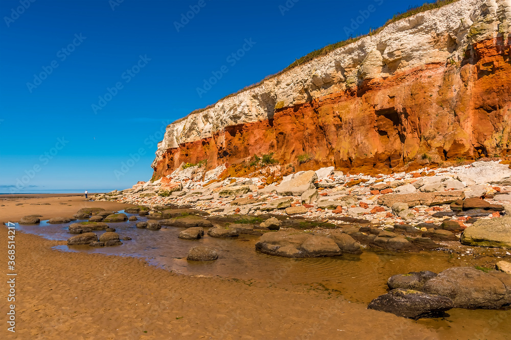 Rockfall of varying colours as the chalk and sandstone erode from the white, red and orange stratified cliffs at Old Hunstanton, Norfolk, UK