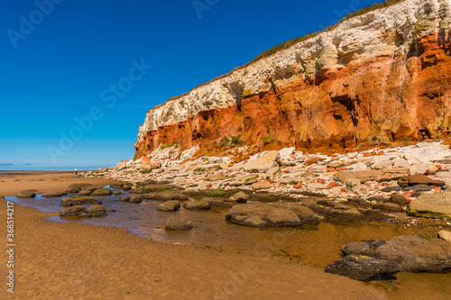 Rockfall of varying colours as the chalk and sandstone erode from the white, red and orange stratified cliffs at Old Hunstanton, Norfolk, UK