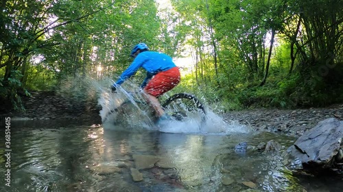 Man on bike crossing mountain river with water splashes slow motion.