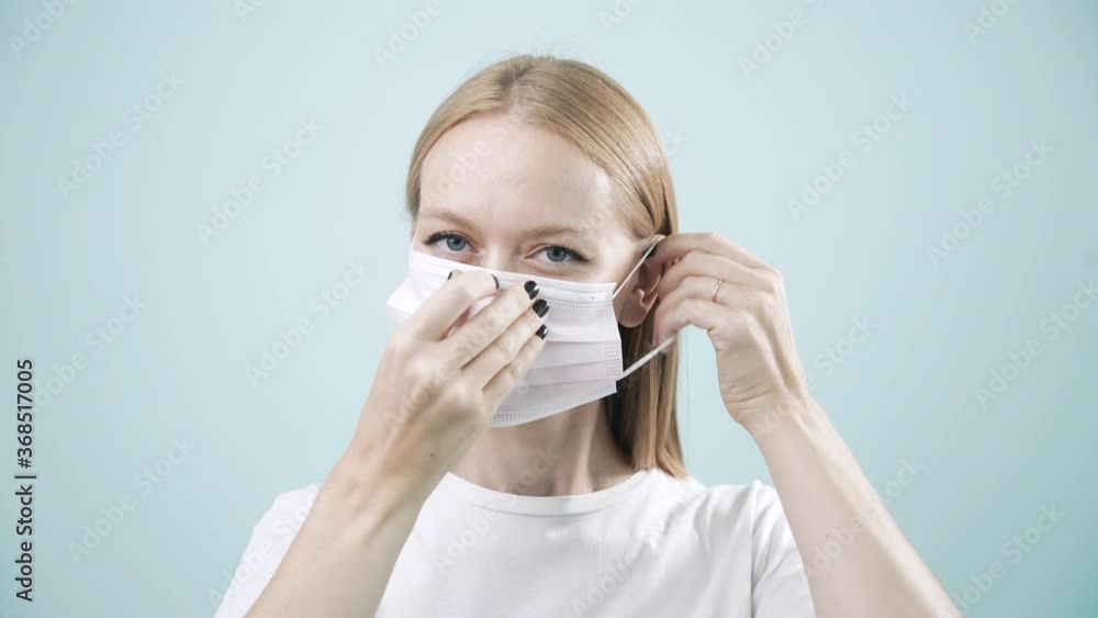 Young woman putting on face medical mask against virus bacteria prevention outbreak on light background. Health protection Corona Virus concept, Covid-19 pandemic. Health care, close up portrait, 4k Young woman putting on face medical mask against virus bacteria prevention outbreak on light background. Health protection Corona Virus concept, Covid-19 pandemic. Health care, close up portrait, 4k