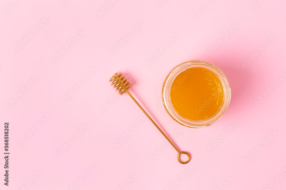 Honey in a glass jar and a golden honey spoon nearby on a pink background. View from above. Honey in a glass jar and a golden honey spoon nearby on a pink background. View from above.