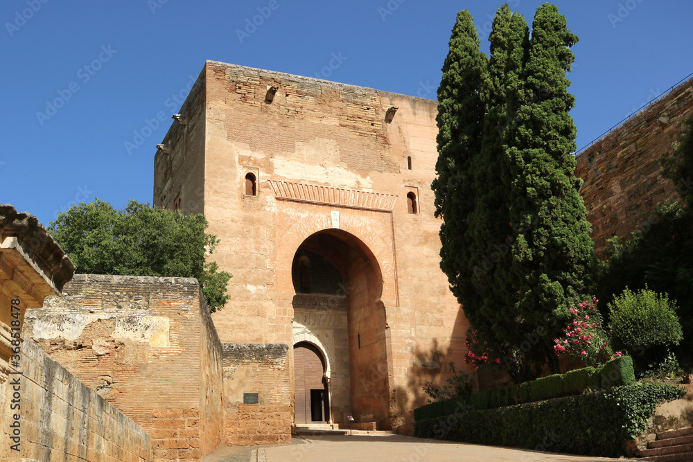 entrance of Alhambra of Granada with wall, muslim arch, trees around and a blue sky
