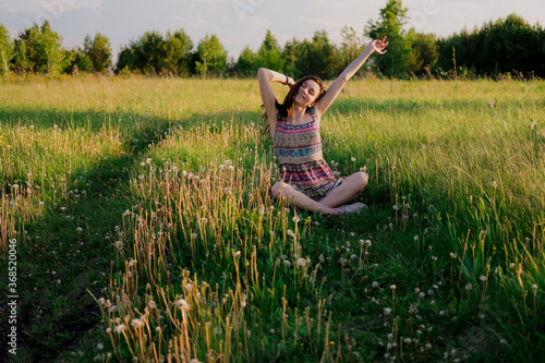 Young woman practicing yoga sitting in easy pose outdoors in green field. Unity with nature concept.