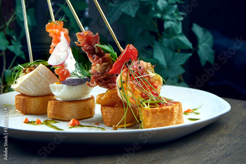 Classic Spanish antipasto - pintxos or tapas with shrimp, camembert, salmon and jamon in a white plate. Selective focus photo