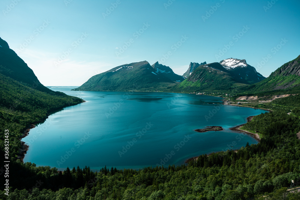 Amazing fiord view. Deep beautiful blue and azure water, green mountains, curving road in the valley. Norwegian natural landscape. Popular tourists place on Senja island, north Norway. 