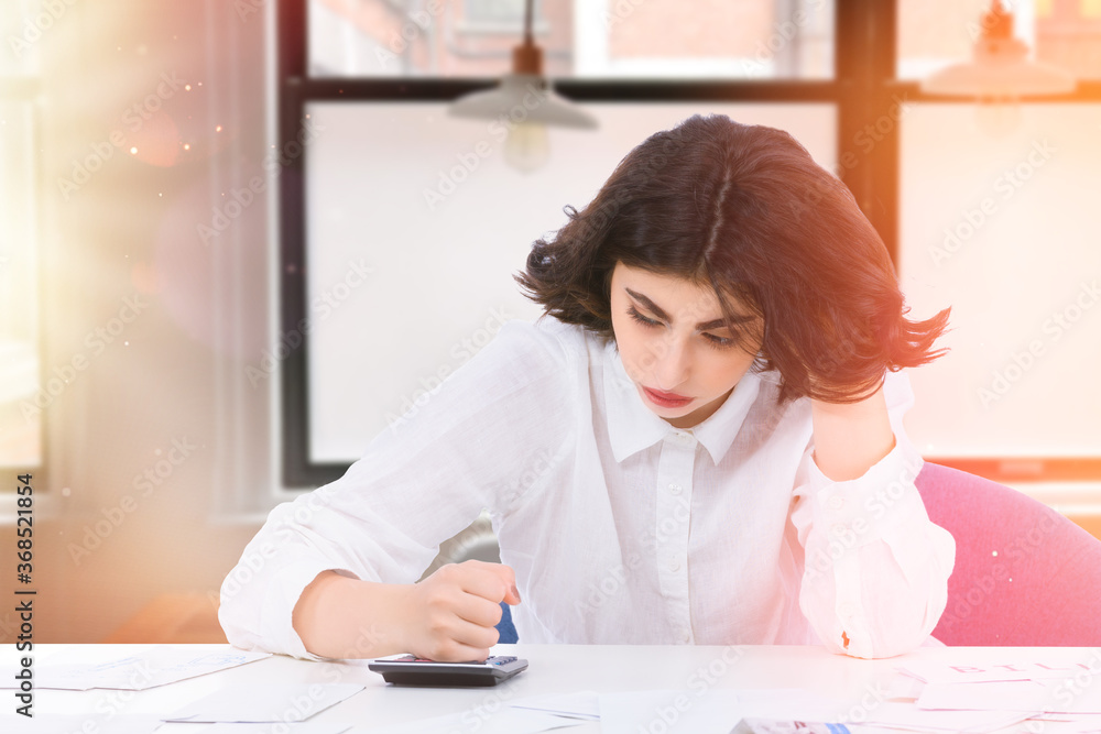 Shot of stressed young woman hitting a calculator with her fist, thinking of financial troubles. Lost in negative thoughts depressed woman worrying about bad news notice. Shot of stressed young woman hitting a calculator with her fist, thinking of financial troubles. Lost in negative thoughts depressed woman worrying about bad news notice.
