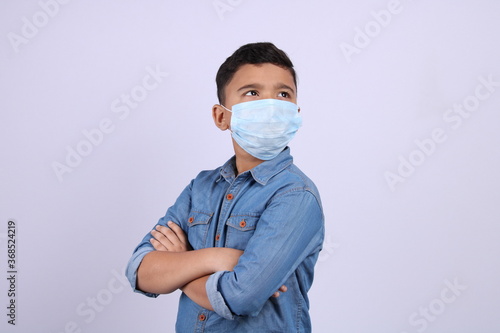 Cute little Indian boy with folded hands wearing surgical mask, looking up, isolated over white background