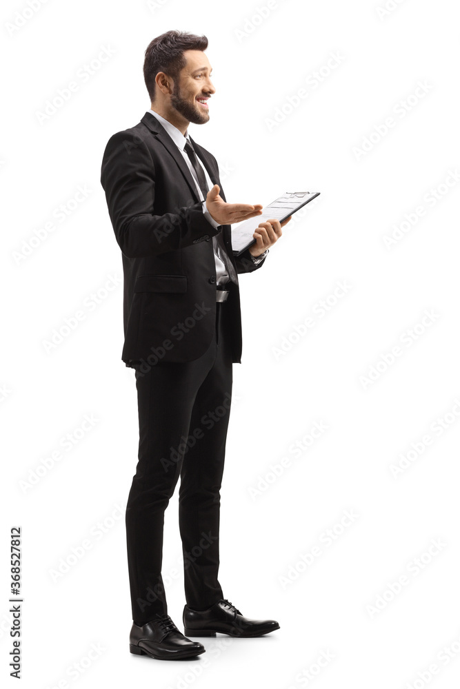 Man in a black suit gesturing with hand and holding a clipboard Man in a black suit gesturing with hand and holding a clipboard