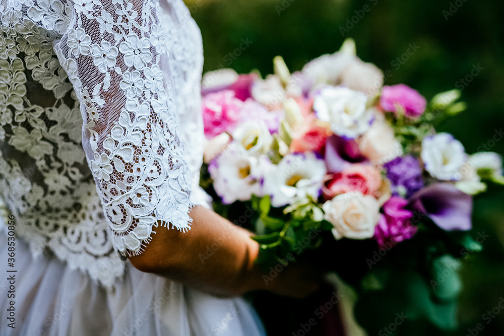 Bridal bouquet, hold the wedding bouquet in your hand, satin ribbons adorn the wedding bouquet of roses, on the background of the bride's dress, fresh flowers, made by a florist Bridal bouquet, hold the wedding bouquet in your hand, satin ribbons adorn the wedding bouquet of roses, on the background of the bride's dress, fresh flowers, made by a florist