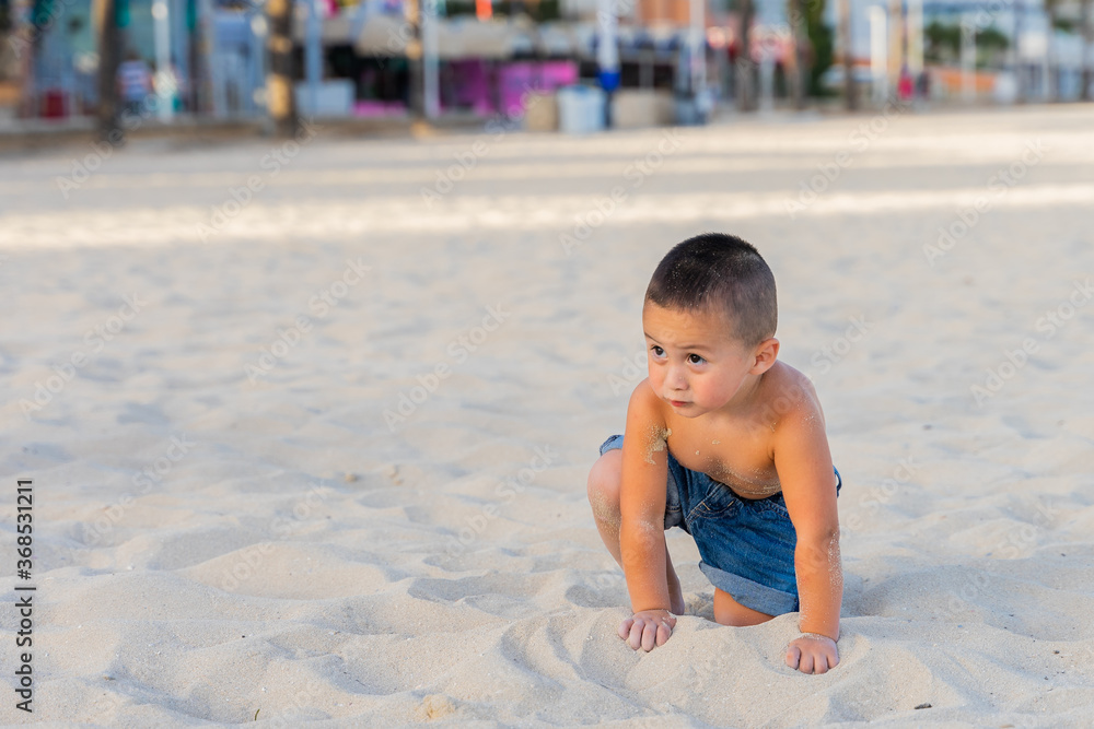 Latin American cute little boy crouched in the sand on the beach, in Mallorca, Spain. Latin American cute little boy crouched in the sand on the beach, in Mallorca, Spain.