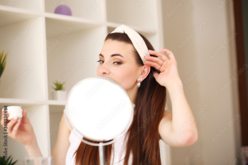 beauty, skincare young woman applying face cream and looking in mirror in home bathroom. beauty, skincare young woman applying face cream and looking in mirror in home bathroom.