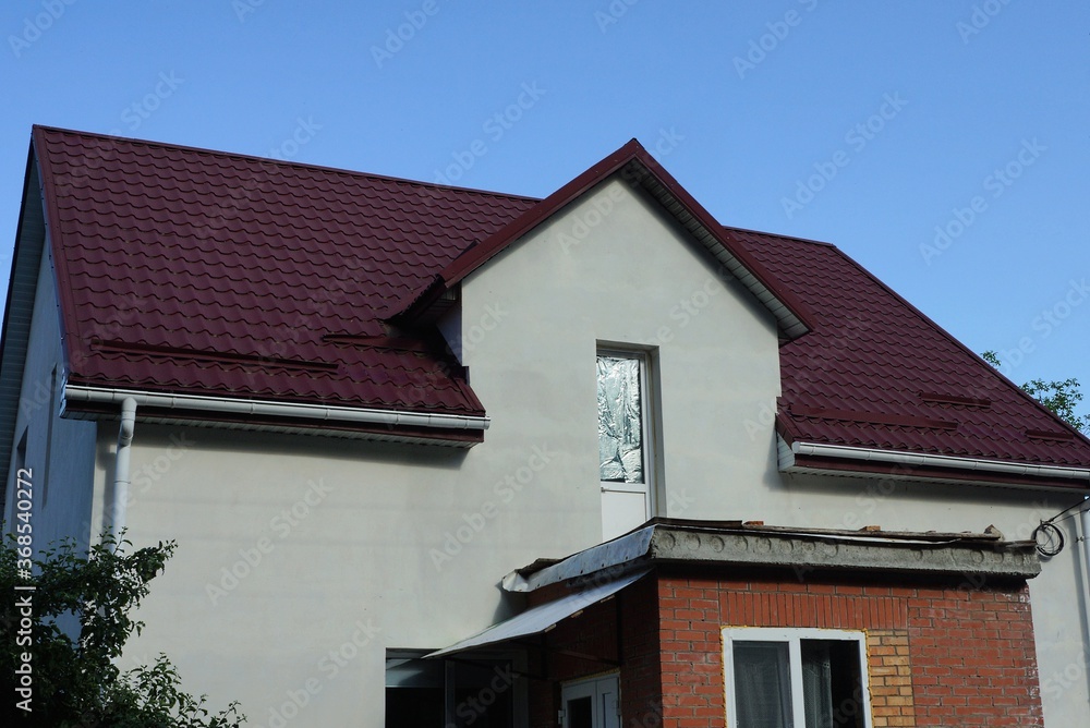 attic of a white private house with a glass door under a red tiled roof against a blue sky
