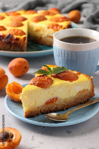 Cheesecake with apricots with a cut out piece  located on a blue plate and cup of coffee  vertical format  Closeup