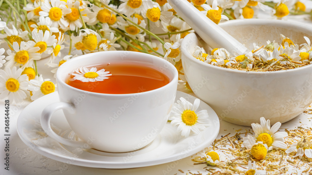Herbal tea of chamomile flower, dried daisies buds in a mortar and a bouquet of Matricaria chamomilla on a concrete background. Healthy tea concept. - obrazy, fototapety, plakaty 