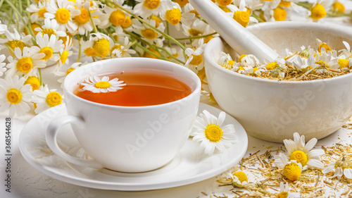Herbal tea of chamomile flower, dried daisies buds in a mortar and a bouquet of Matricaria chamomilla on a concrete background. Healthy tea concept.