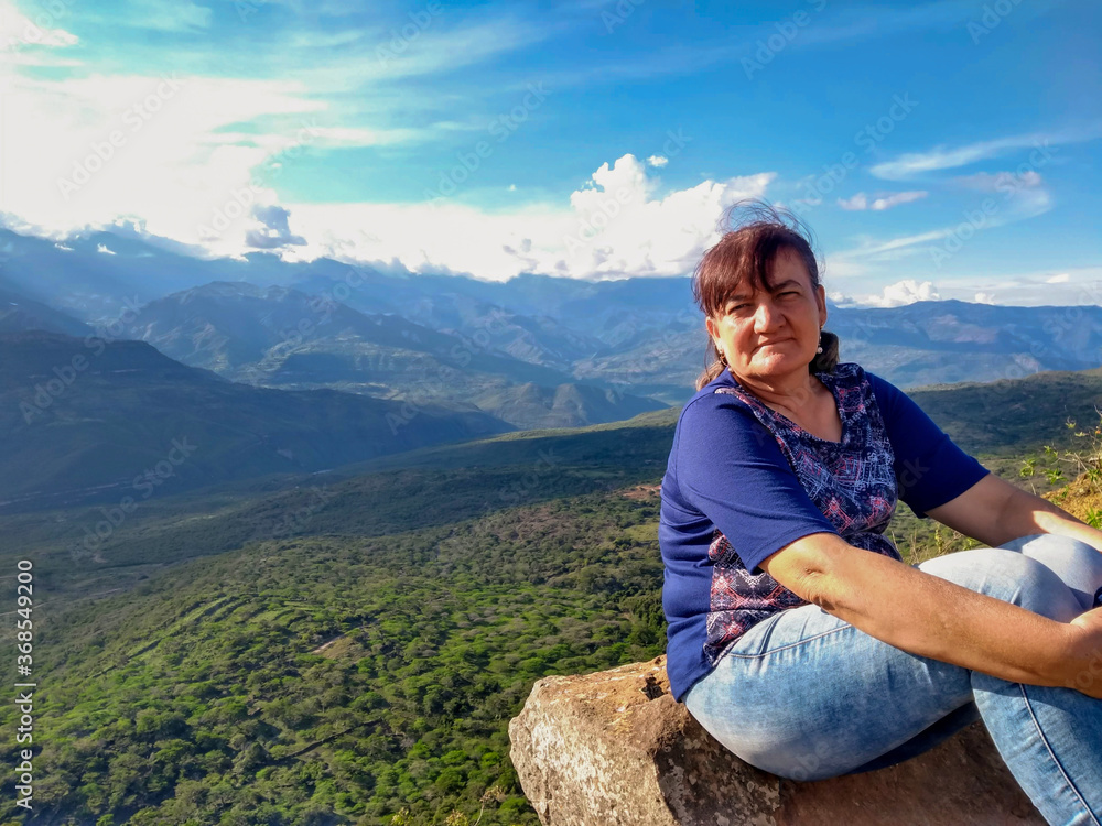 Naklejka premium mujer mayor sentada en una roca en el borde del acantilado con un hermoso paisaje 