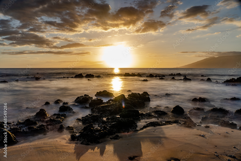 Sunset on beach in Hawaii Maui Long exposure of waves coming in. Sun bright coming down