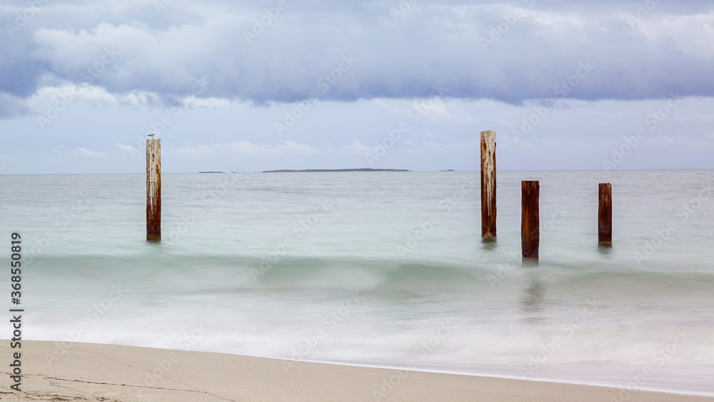 Old wooden jetty posts in the ocean on a cloudy day
