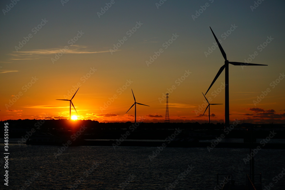 Beautiful sunset at jetty over the water with windmills and industrial shipping.
