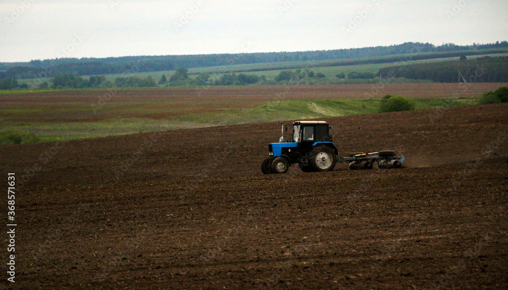 Obraz premium large tractor with plow plows field before spring sowing of crops. tractor with harrow drives across plowed field and levels arable land.