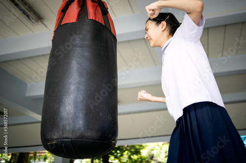 Angry asian child girl is crying and raising fists,woman is hitting punches into the punching bag to release resentment,emotional explosion,stress relief,venting anger,outbursts of violence,catharsis
