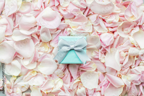 Gift box lying on Rose petals pink color closeup, holiday background.