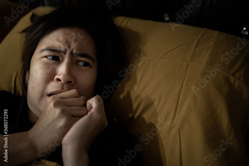 Frightened woman is looking around while lying on her bed,feeling anxious,afraid of shaking,hearing something haunting,symptoms of phobia,hallucinations,sleep deprivation or insufficient sleep chronic