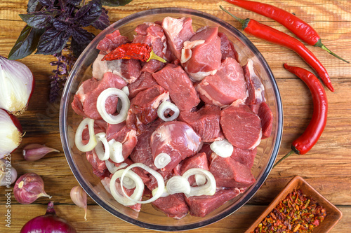 Boneless lamb steak, sliced and marinated with onions, meat in a glass bowl, Basil, chili peppers, marinades on a wooden table, top view, close-up.