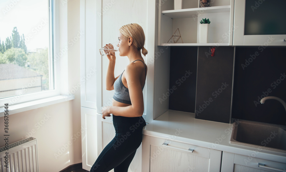 Lovely blonde woman drinking a glass of water wearing sportswear at home Lovely blonde woman drinking a glass of water wearing sportswear at home