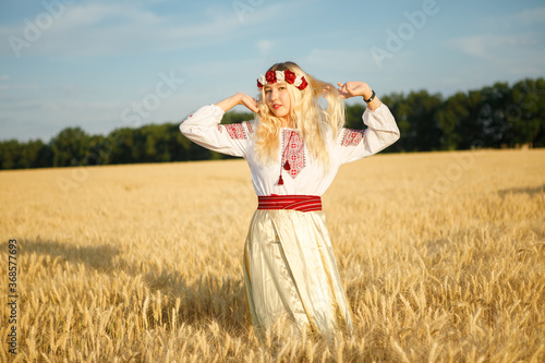 Young white woman with long blondy hair dressed a white dress in a wheat field