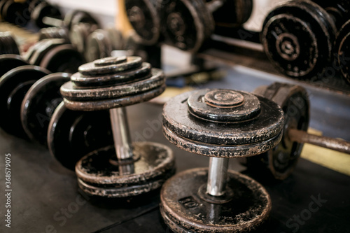 A clutter of heavy, rusty dumbbells in front of a dumbbell rack. A mess of weights at the gym. photo