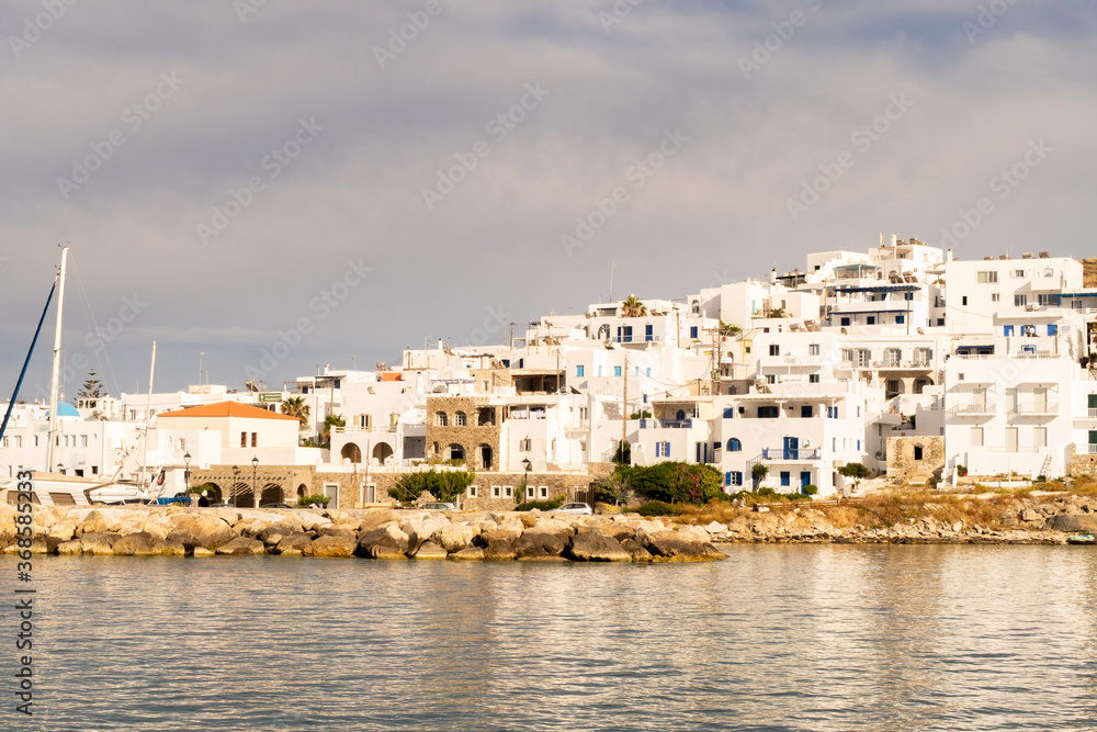 Naoussa coastal village (Paros Island) landscape view during golden hour with typical whitewashed cycladic houses and dramatic sky seen from the sea, Greece.