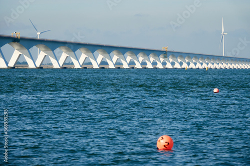 Long Zeeland Bridge, deep blue water with a red buoy, wind turbine in the background. Netherlands, Zeeland. © Jan