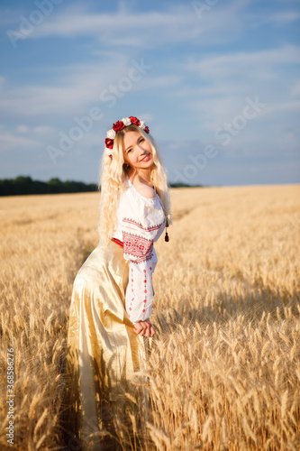 Young european woman with long blond hair in a white dress in a wheat field