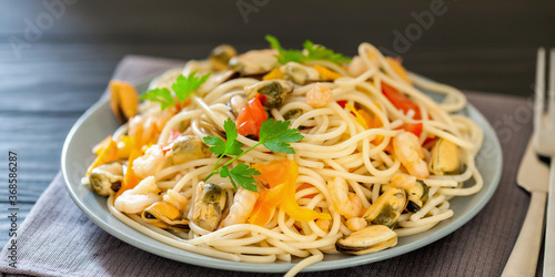 Seafood noodles. Pasta with seafood and vegetables - shrimps, mussels, tomato and spinach on a dark background. Selective focus