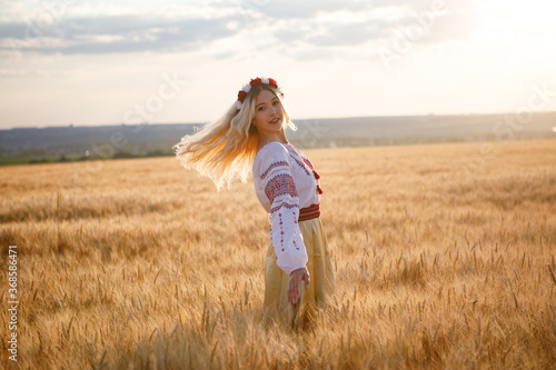 Young european woman with long blond hair in a white dress in a wheat field