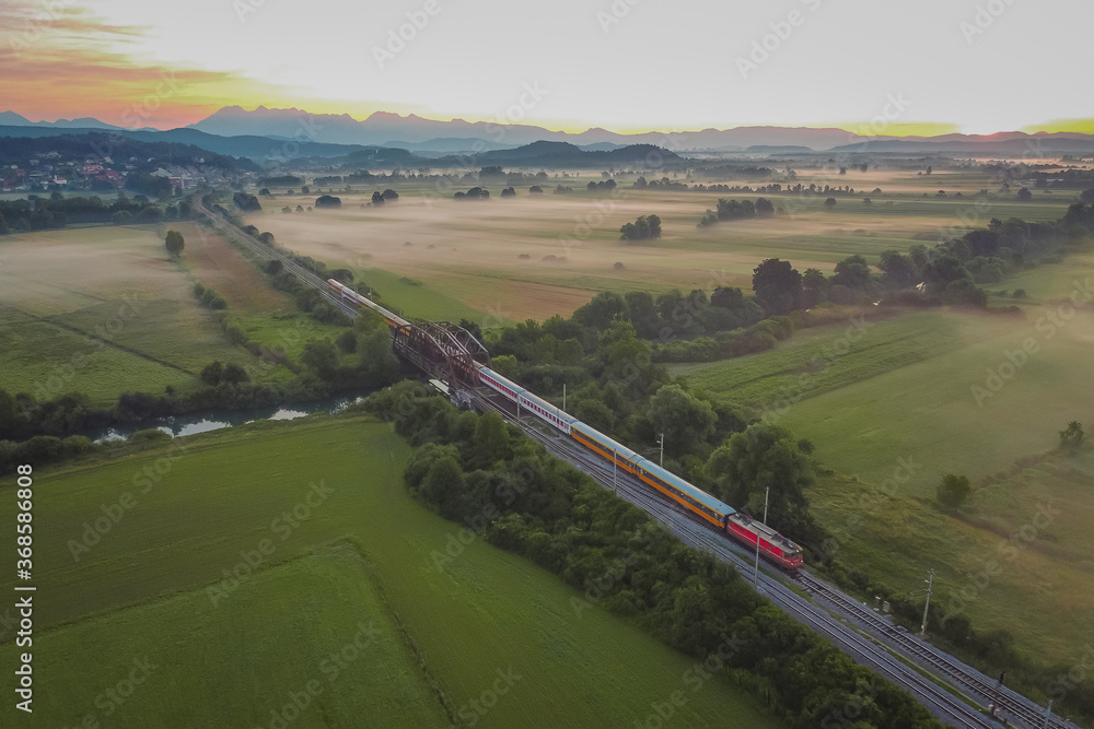 Express passenger train from Prague to Rijeka on its way over the Ljubljana marshes in early romantic morning with sunrise.