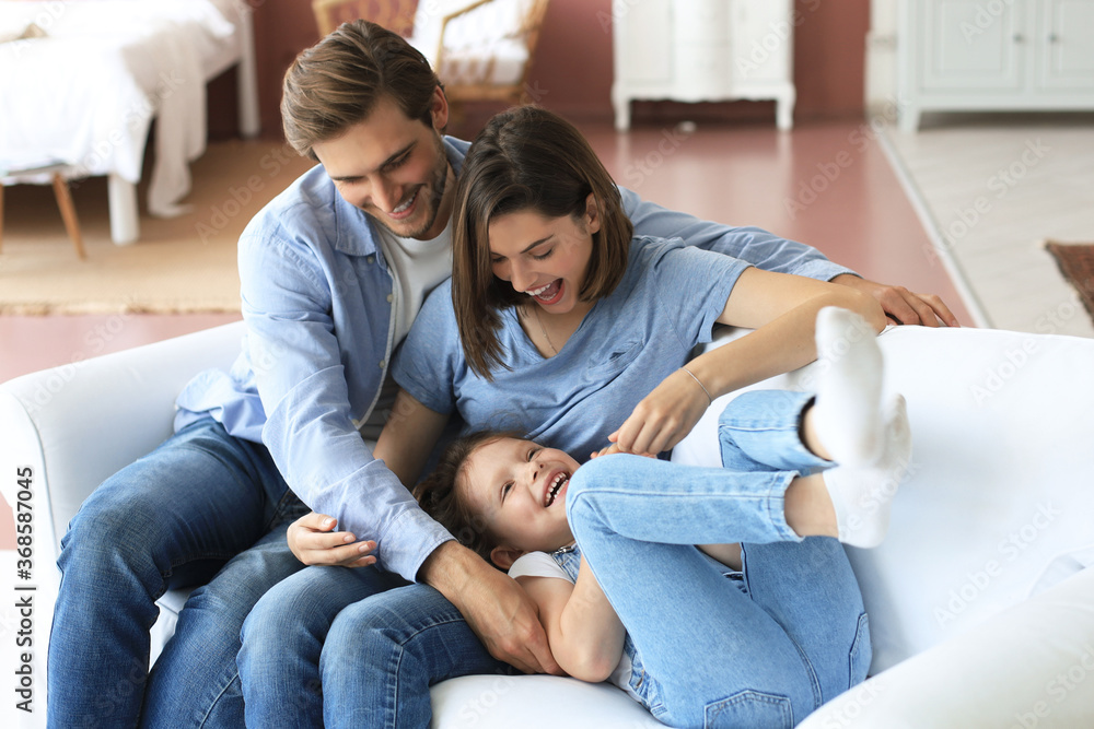 Positive friendly young parents with smiling little daughter sitting on sofa and having fun together at home. Positive friendly young parents with smiling little daughter sitting on sofa and having fun together at home.